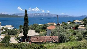 Un pueblo costero con casas, un ciprés alto y vistas al mar y las montañas.
