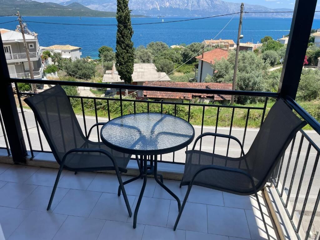 A balcony with a round table and two chairs, overlooking a body of water and mountains.