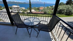 Un balcón con una mesa redonda y dos sillas, con vista a un paisaje costero con edificios y montañas.