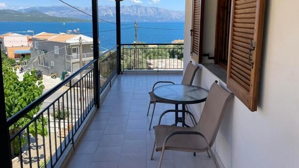 Un balcón con mesa y sillas, con vista al agua y montañas.
