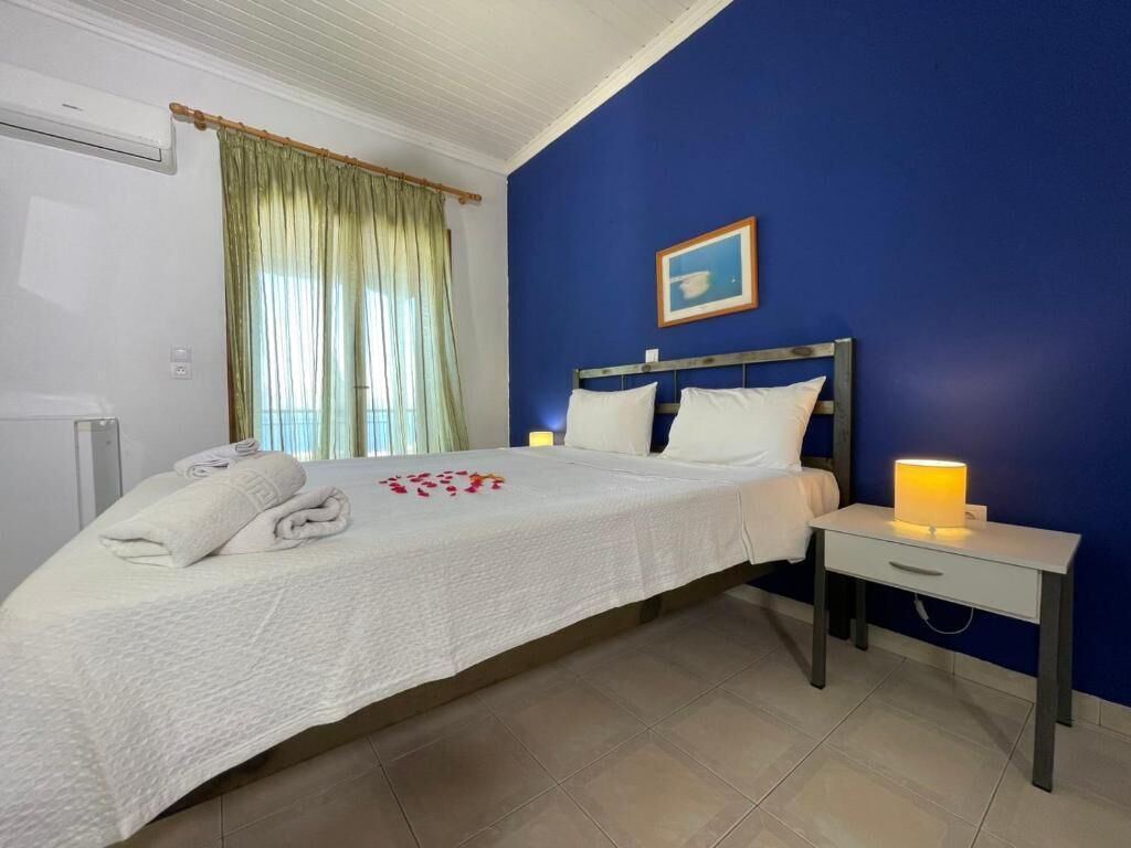 Un dormitorio con cama, mesita de noche con lámpara, ventana con cortinas y un cuadro en la pared.