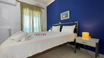 Un dormitorio con cama, mesita de noche con lámpara, ventana con cortinas y un cuadro en la pared.