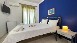Un dormitorio con cama, mesita de noche, lámpara, aire acondicionado, televisor y una ventana con cortinas.
