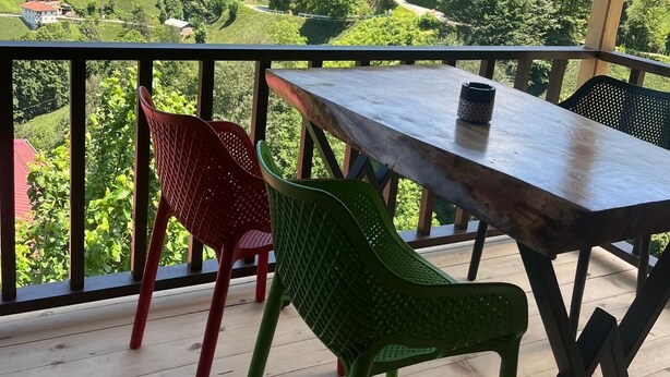 A wooden deck with a table and two chairs, overlooking a mountainous landscape with houses. - Derya Dağ Evi (Çamlıhemşin)
