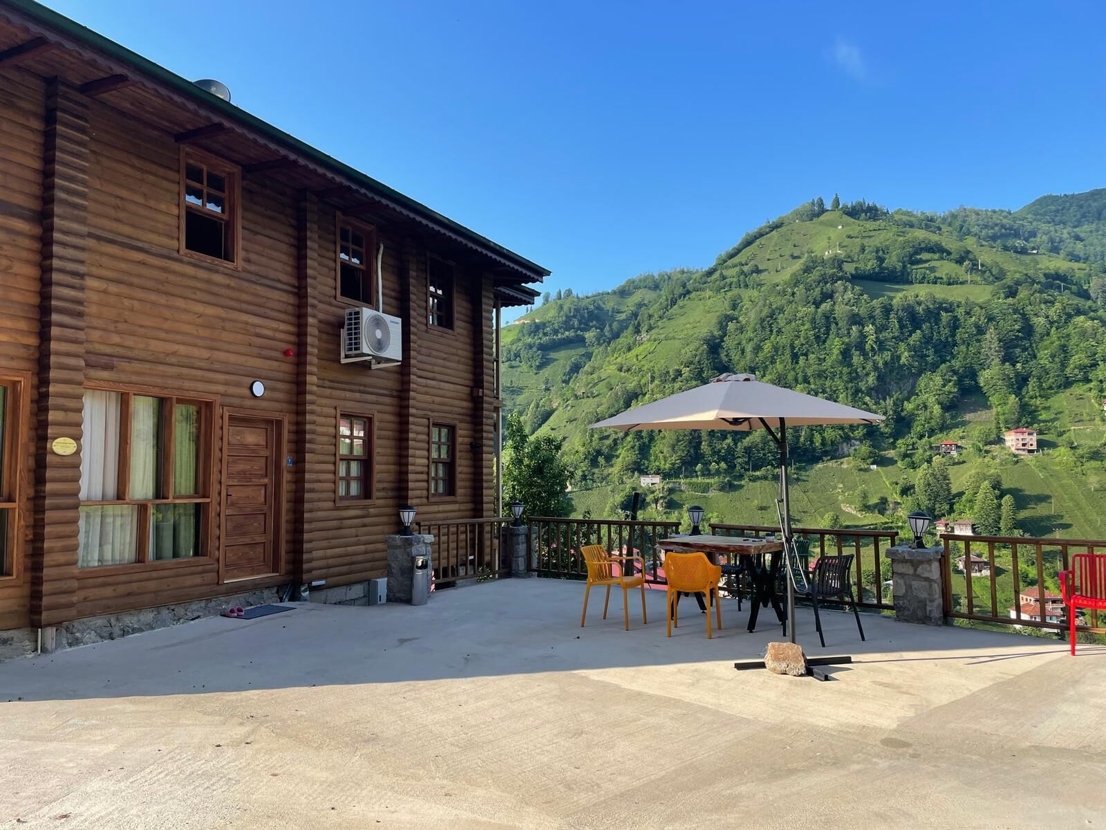 A wooden building with a balcony, outdoor seating, and a mountain view.