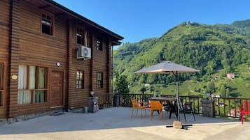 A wooden building with a balcony, outdoor seating, and a mountain view.