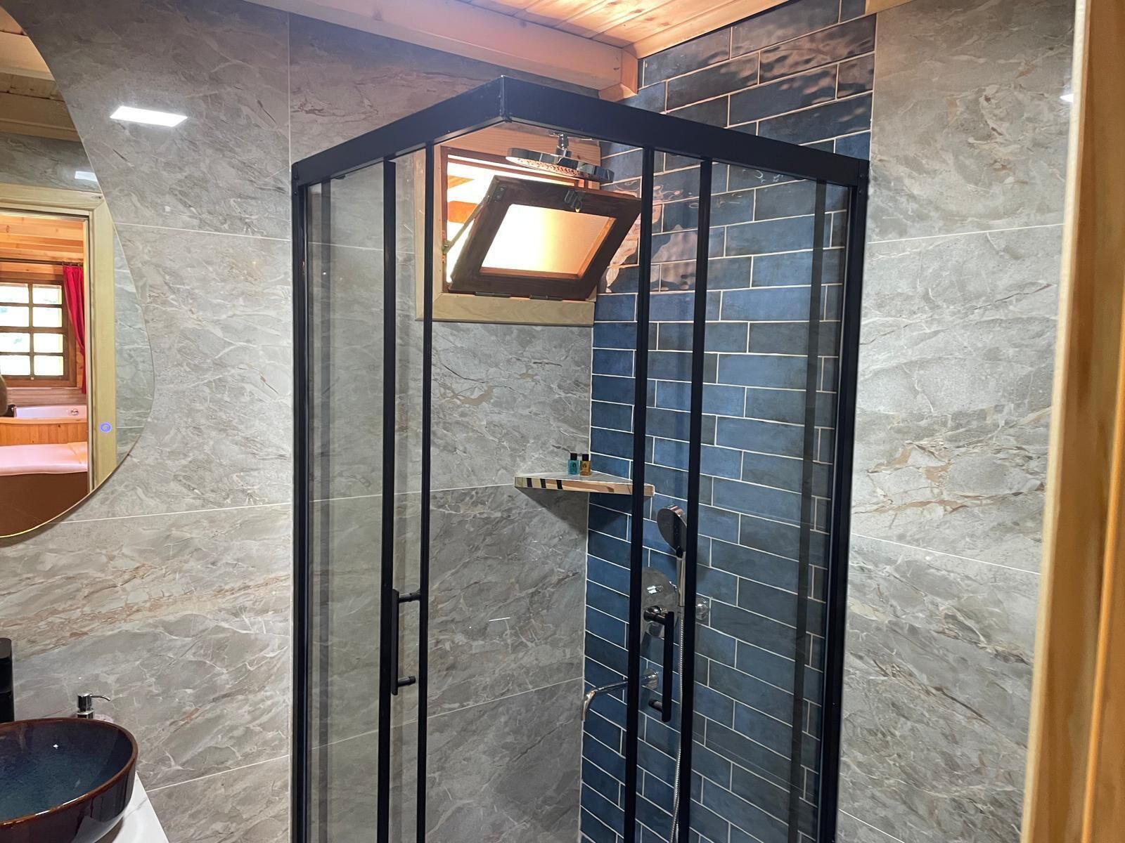 Un baño moderno con ducha de vidrio, paredes de mármol y tocador de madera.