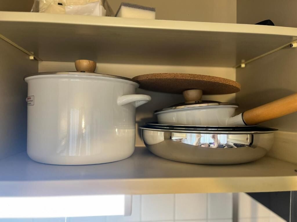 Une étagère de cuisine avec des pots en céramique blanche et un ustensile de cuisine dont le manche est en bois.