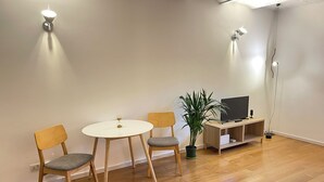 Ein Zimmer mit einem runden Tisch, zwei Stühlen, einem Fernseher auf einem Holzschrank und einer Pflanze.
