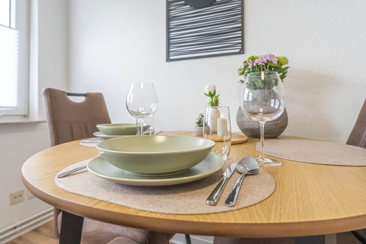 Une table à manger dressée avec de l’assiette verte, des couverts en argent et des verres à vin, agrémentée d’un vase de fleurs et d’une bougie.