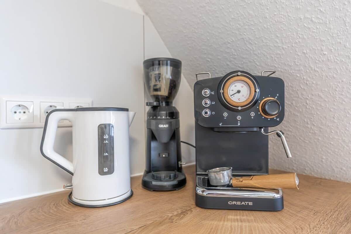 Een koffiezetapparaat, een waterkoker en een koffiemolen op een houten aanrecht.