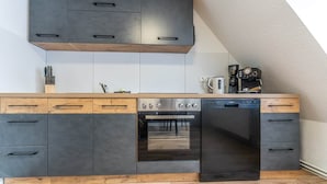 A kitchen with dark cabinets, a dishwasher, an oven, and a coffee maker. - Bright & Cozy Apartment with Harbor View in Varel (Varel)