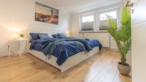 A bedroom with a bed, a bedside table, a lamp, a window, and a potted plant. - Bright & Cozy Apartment with Harbor View in Varel (Varel)