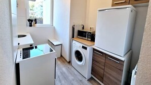 Ett kompakt kök med tvättmaskin, mikrovågsugn och kylskåp.