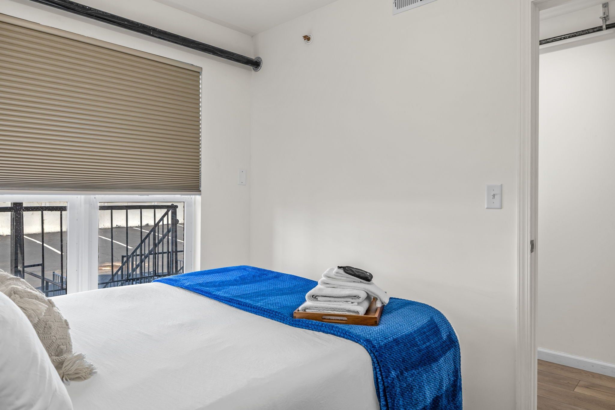 A bedroom with a bed, a blue blanket, and a stack of towels on a wooden tray.