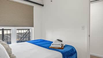 A bedroom with a bed, a blue blanket, and a stack of towels on a wooden tray.