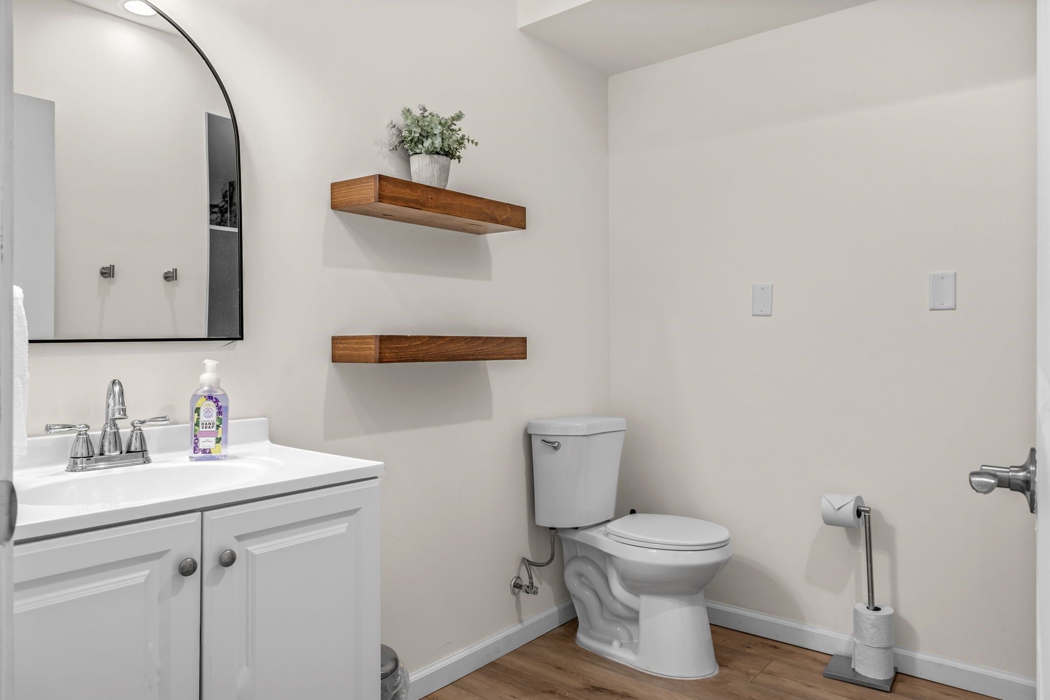 A bathroom with a white sink, mirror, toilet, and wooden shelves.