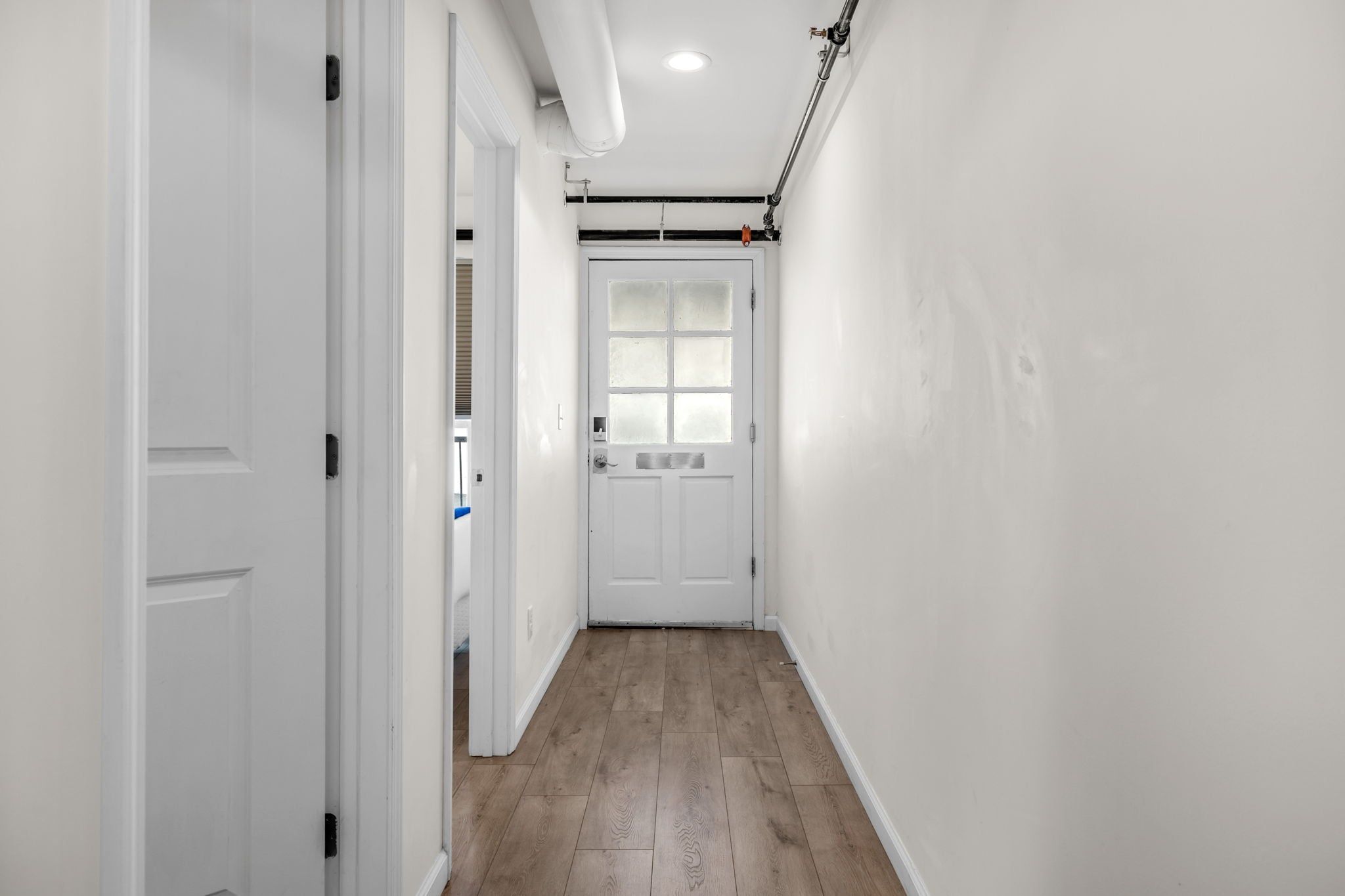 A hallway with white walls, a wooden floor, and a white door at the end.