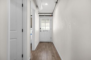 Un pasillo con paredes blancas, suelo de madera y una puerta blanca al final.