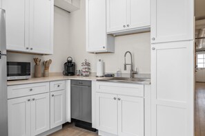 Una cocina moderna con armarios blancos, un lavamanos de acero inoxidable y un microondas.