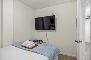 Un dormitorio con una cama, un televisor montado en la pared y una puerta que da a otra habitación.