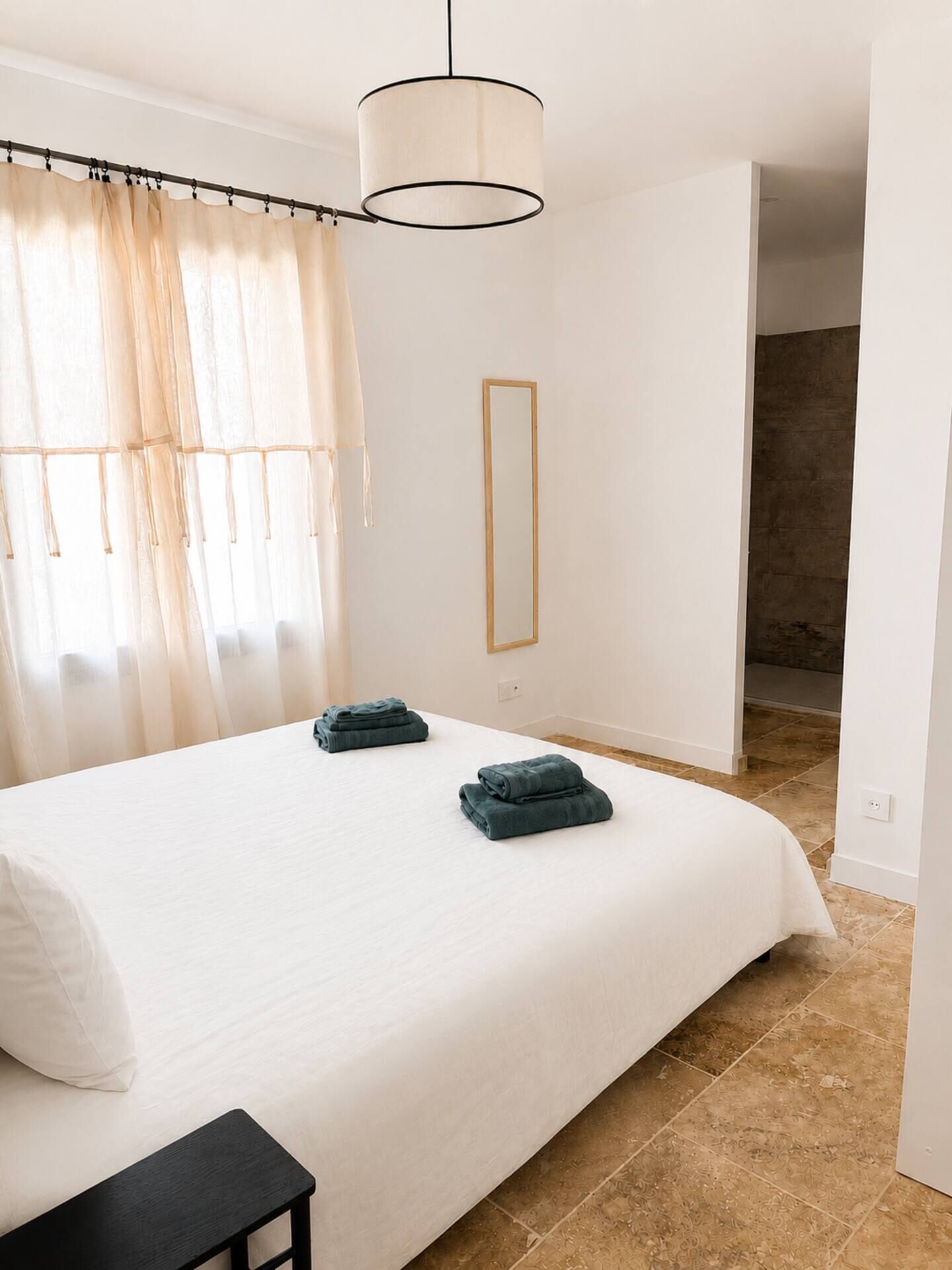 A bedroom with a large bed, a bedside table, a hanging light fixture, a mirror, and a view of a stone wall.