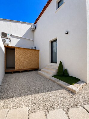A modern building with a white exterior, a wooden deck, and a small garden area with steps leading to a door. - New villa with a private pool • 3 bedrooms with private bathrooms (Clarensac)