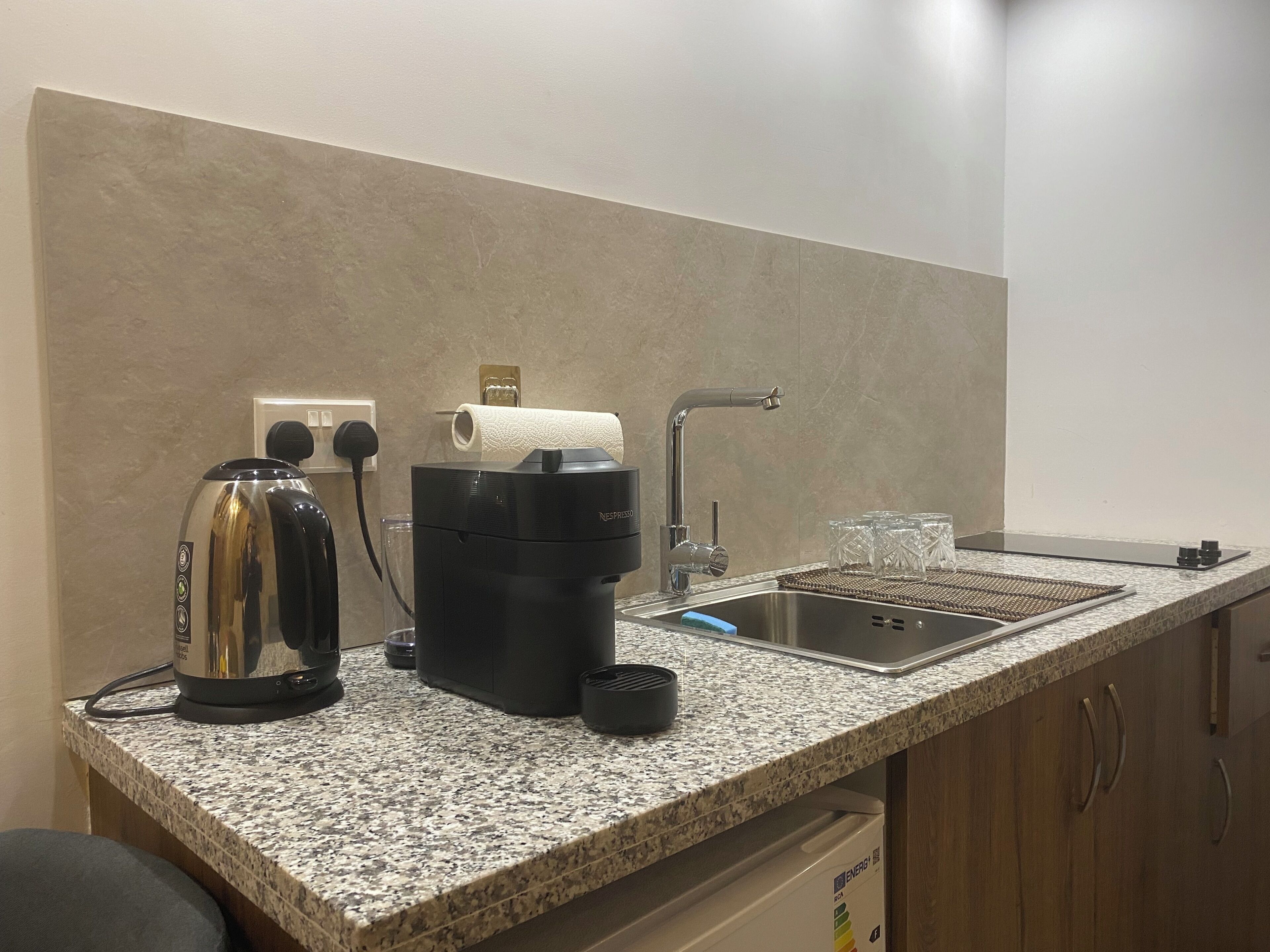 A kitchen with a granite countertop, a coffee maker, a kettle, a sink, and a dish rack.