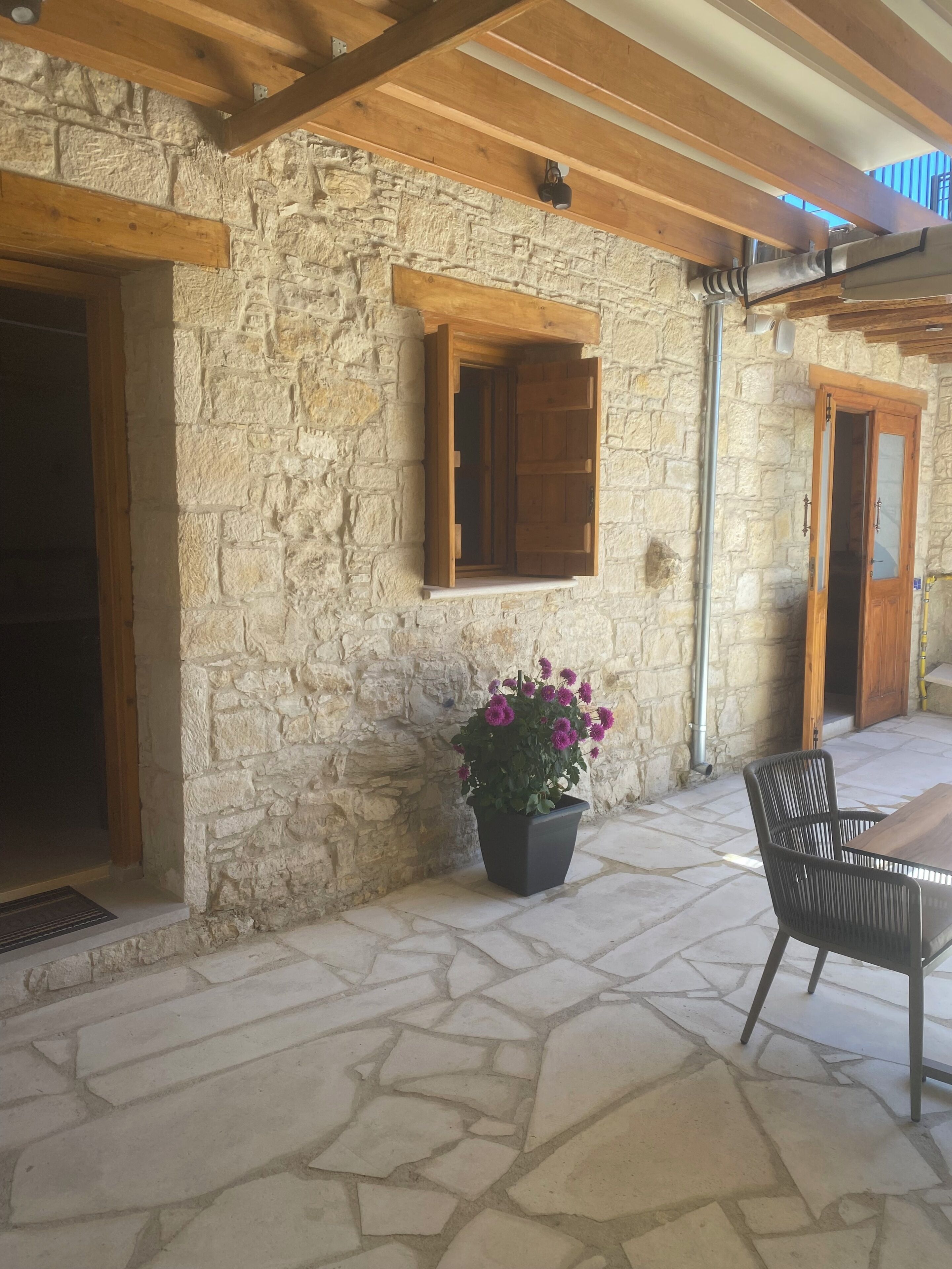 A stone building with a wooden door, a window with a wooden shutter, and a potted plant with purple flowers.