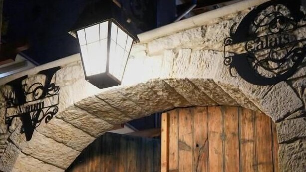 A wooden door with a stone archway, a lantern, and a sign above the door. - Vouni Calais  (Vouni)