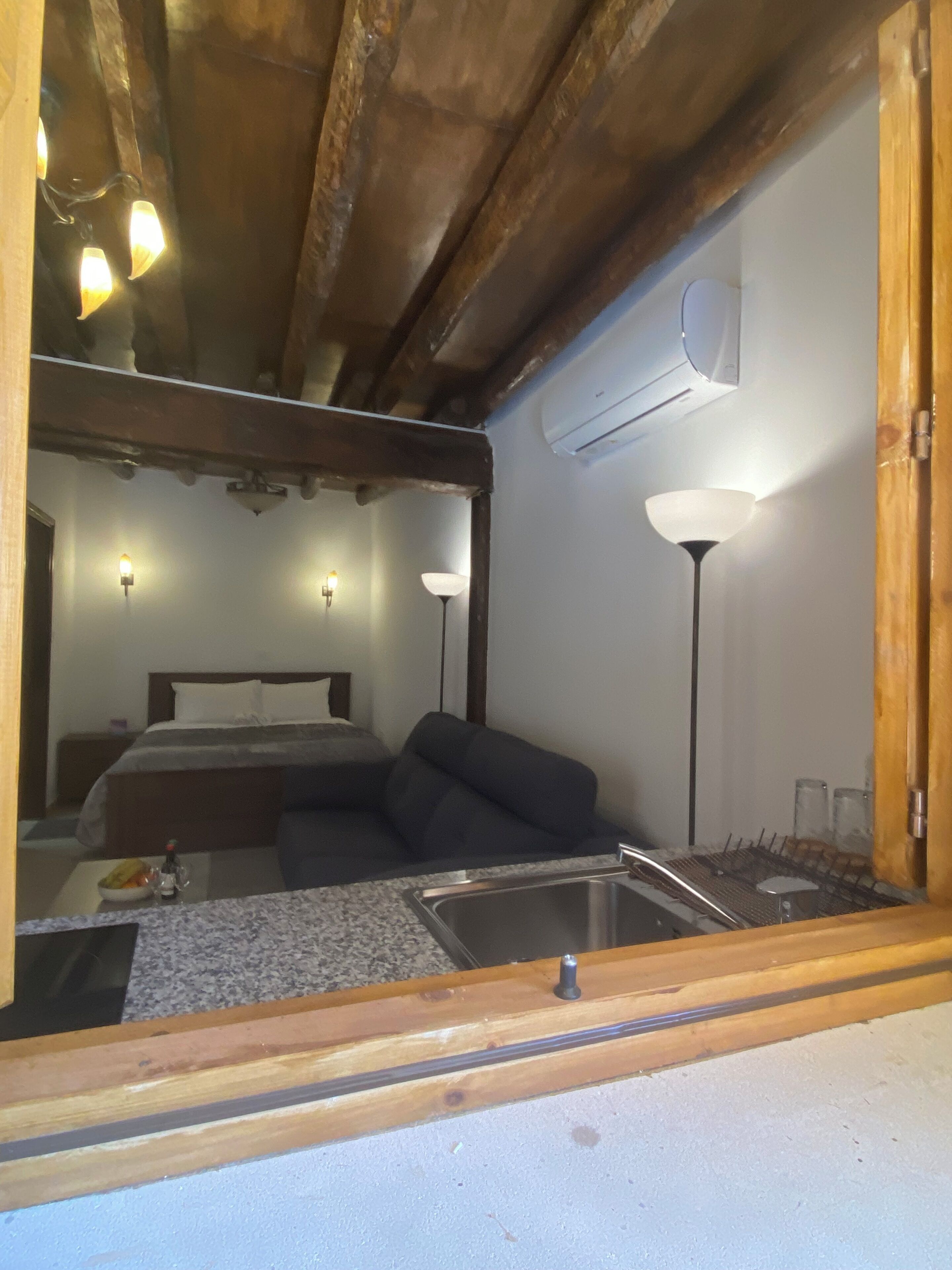 Habitación de hotel compacta con cama, sofá, pequeña cocina con lavamanos y ventilador de techo.