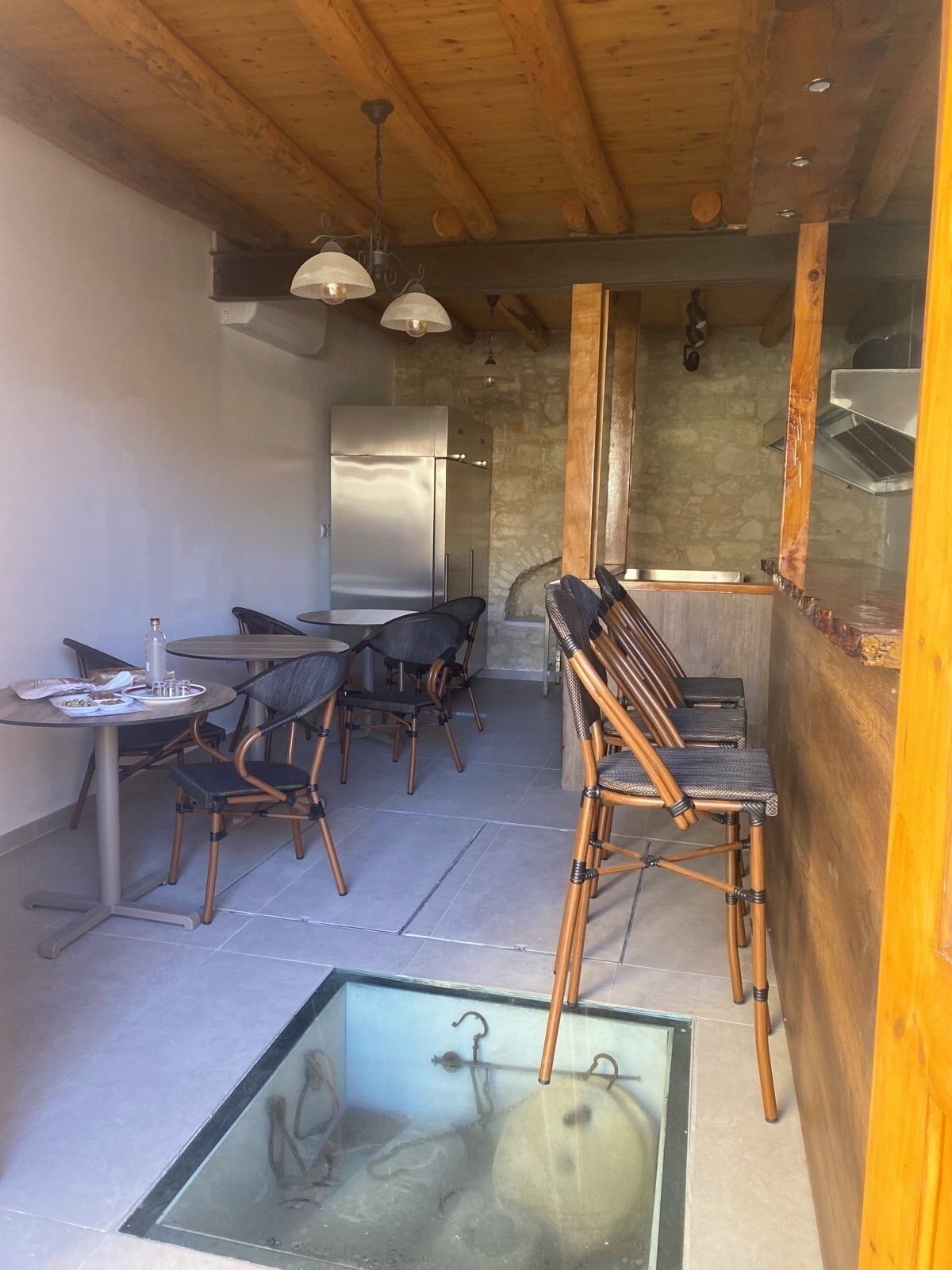 Una cucina rustica con travi in legno, un frigorifero e un'area pranzo con sedie in vimini e un tavolo in vetro.