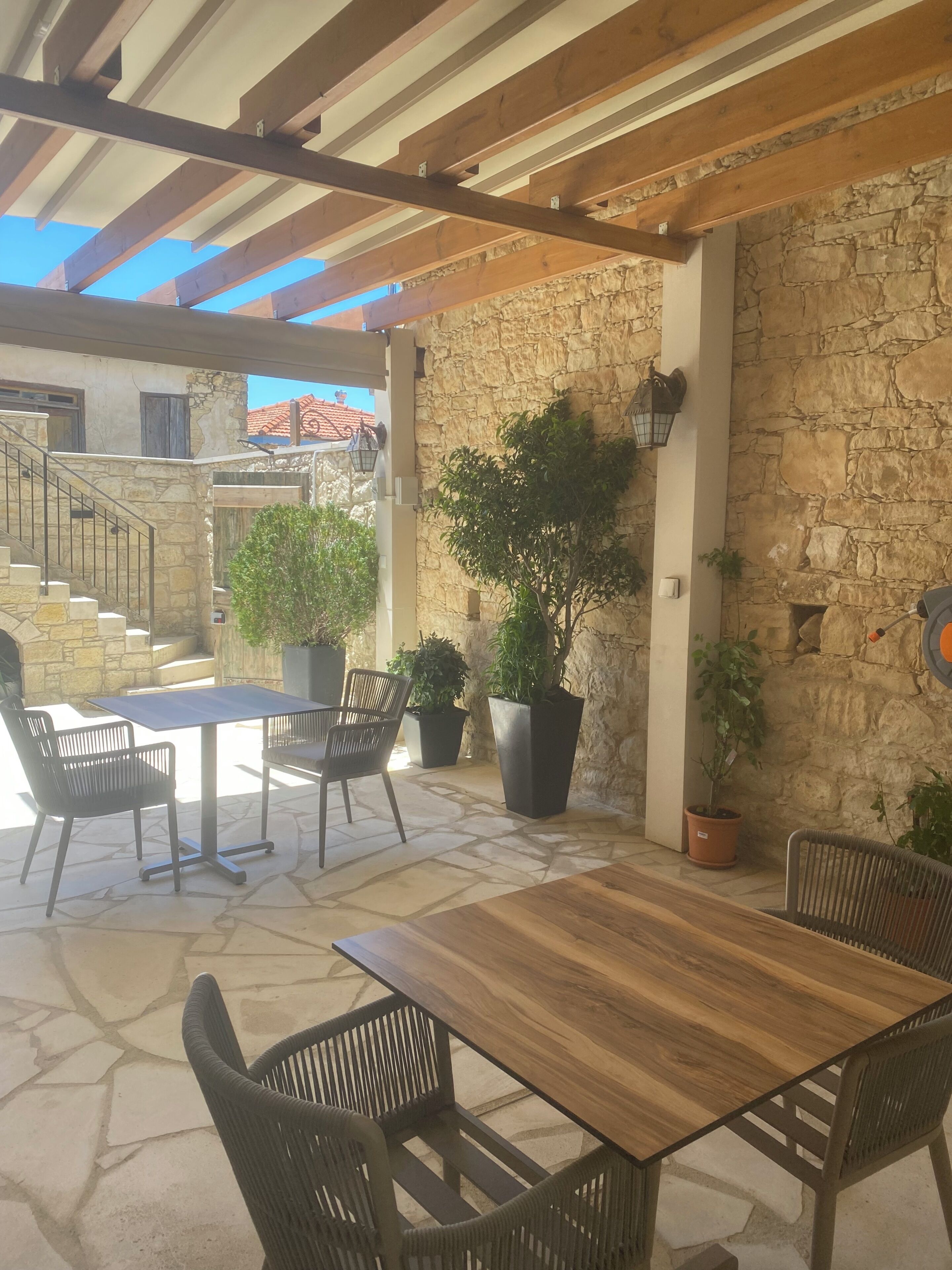 An outdoor patio with a wooden table and chairs, stone walls, and potted plants.