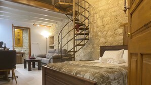 A bedroom with a spiral staircase, a bed with a headboard, a sofa, and a small table with candles. - Vouni Calais  (Vouni)