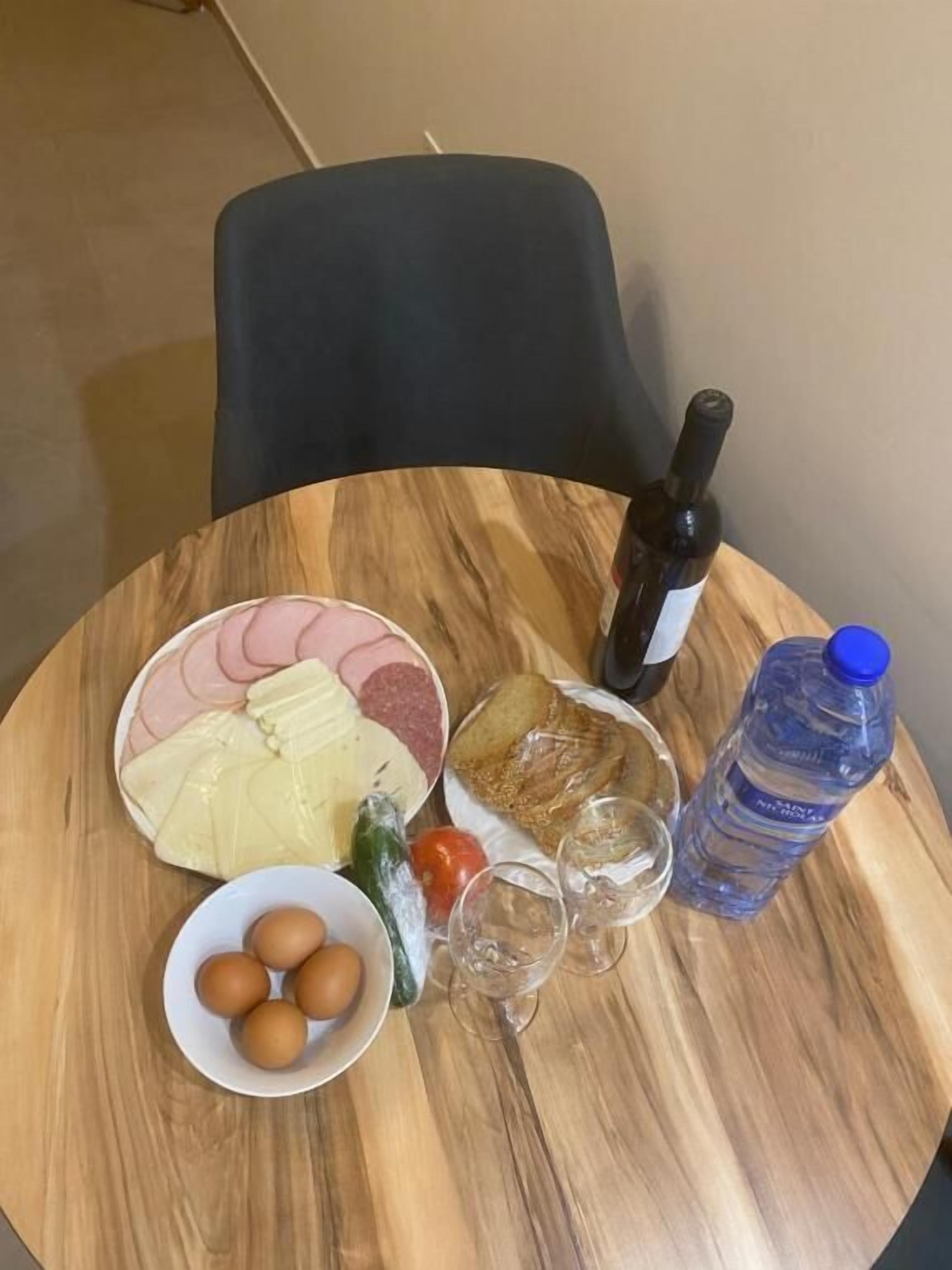 A round wooden table with a plate of food, a bottle of water, and a wine bottle.