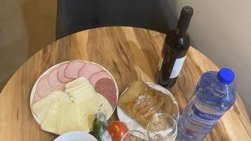 A round wooden table with a plate of food, a bottle of water, and a wine bottle.