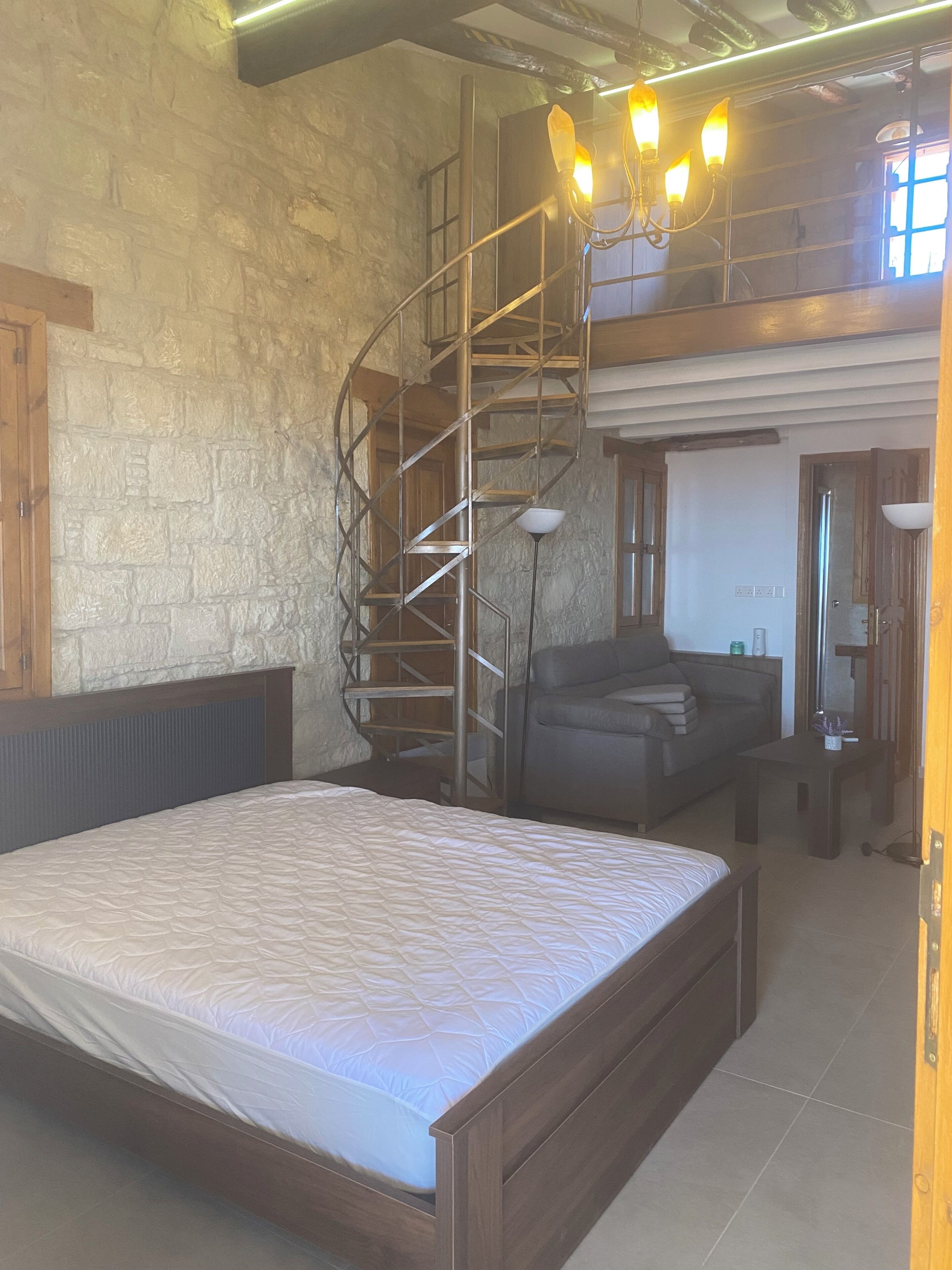 A bedroom with a bed, a staircase, a sofa, and a desk.