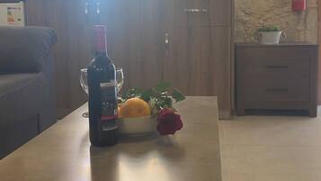 A kitchen with wooden cabinets, a countertop, a bottle of wine, a bowl with an orange and a rose, and a fire extinguisher on the wall.