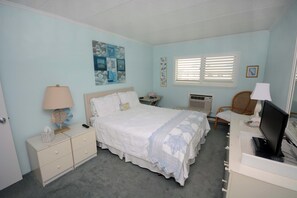 A bedroom with a bed, bedside tables, a desk with a computer, and a window with blinds. - Kitschy 1 Bedroom Oceanfront Condo with Free WiFi, Coastal Decor, and a Breathtaking View Located Uptown and Mere Steps from the Beach! (Ocean City)
