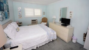 Un dormitorio con cama, cómoda, televisor y obras de arte en las paredes.