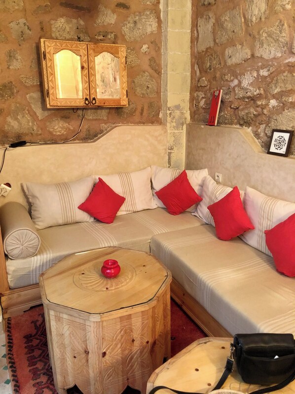 A cozy room with a sofa, a wooden side table, a small red vase, and a black bag. - A small, quiet riad in the heart of the Medina, 150 meters from the city wall (Essaouira)