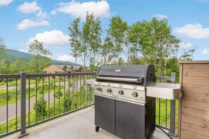A portable gas grill on a balcony with a view of a residential area and hills. - Tremblant Prestige - Verbier 10-203 (Mont-Tremblant)