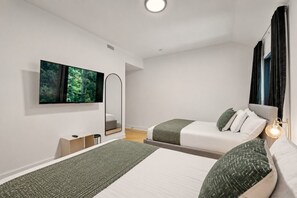 Een moderne hotelkamer met twee bedden, een grote spiegel, een flatscreen televisie en een bedlampje.