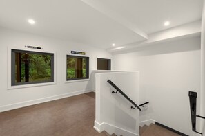 A modern interior with white walls, a staircase with a glass railing, and three windows offering views of greenery. - Tremblant Prestige - Verbier 10-203 (Mont-Tremblant)