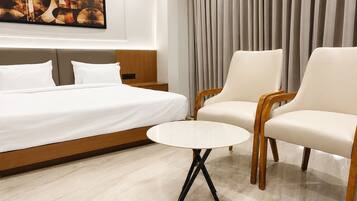 A hotel room with a bed, two armchairs, a small round table, a painting on the wall, and a curtain.
