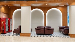 A lobby with a Coca-Cola vending machine, a seating area with brown leather sofas, and a patterned floor. - LUXURIA INN BY CHANDAN (Vanthli)