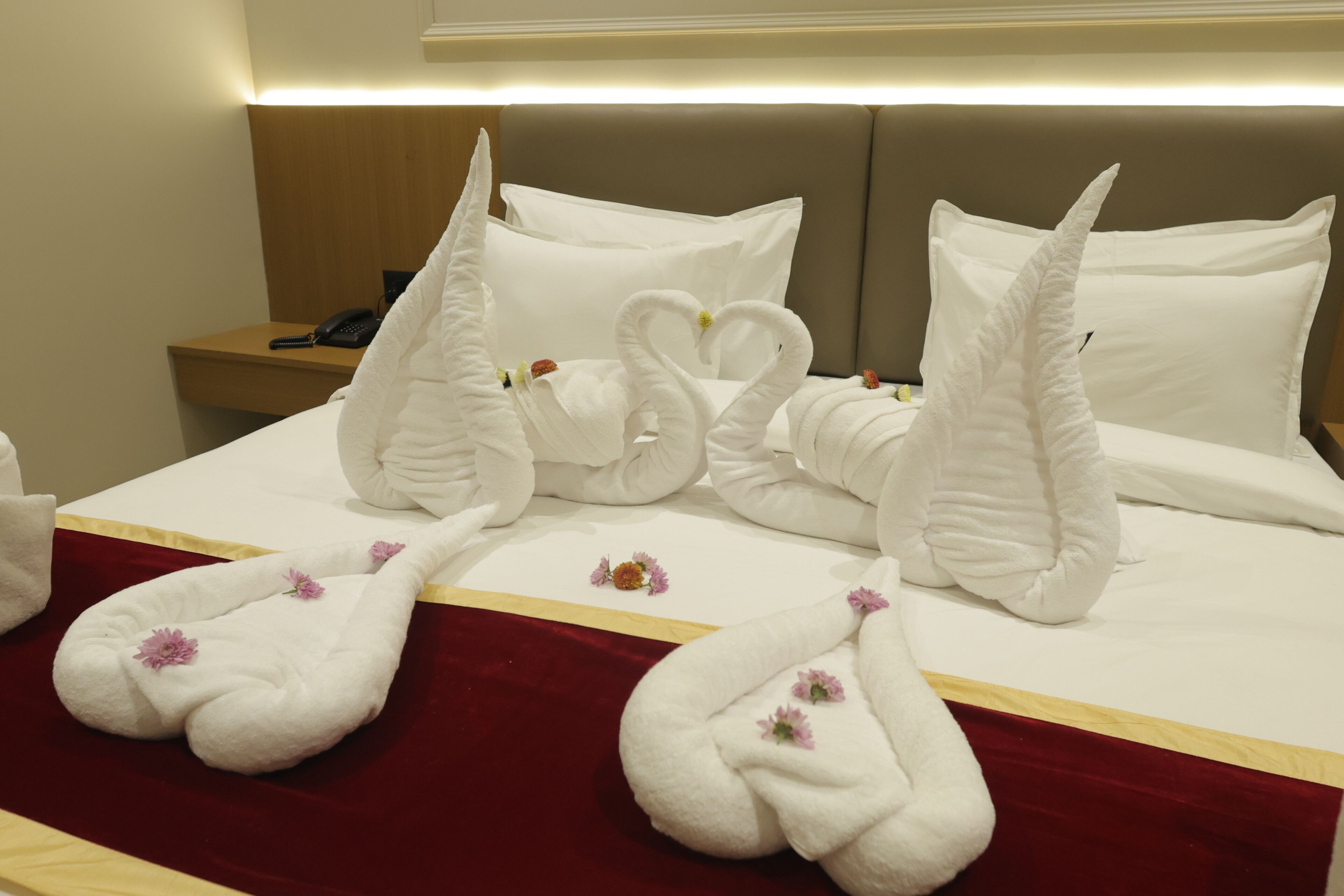 A hotel room with a bed featuring swan-shaped towels and a red bedspread.