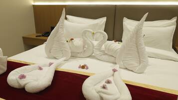 A hotel room with a bed featuring swan-shaped towels and a red bedspread.