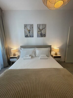 Ein Hotelzimmer mit einem großen Bett, zwei an der Wand befestigten Bildern, Nachttischlampen und einer Tür.
