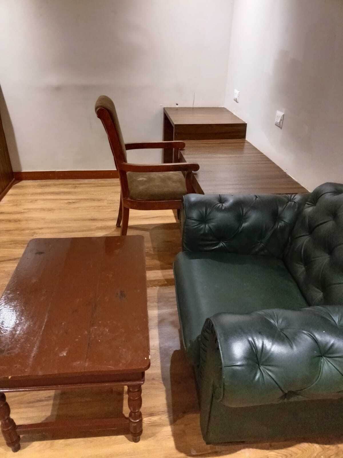 A room with a wooden floor, a wooden chair, a leather sofa, and a wooden table.